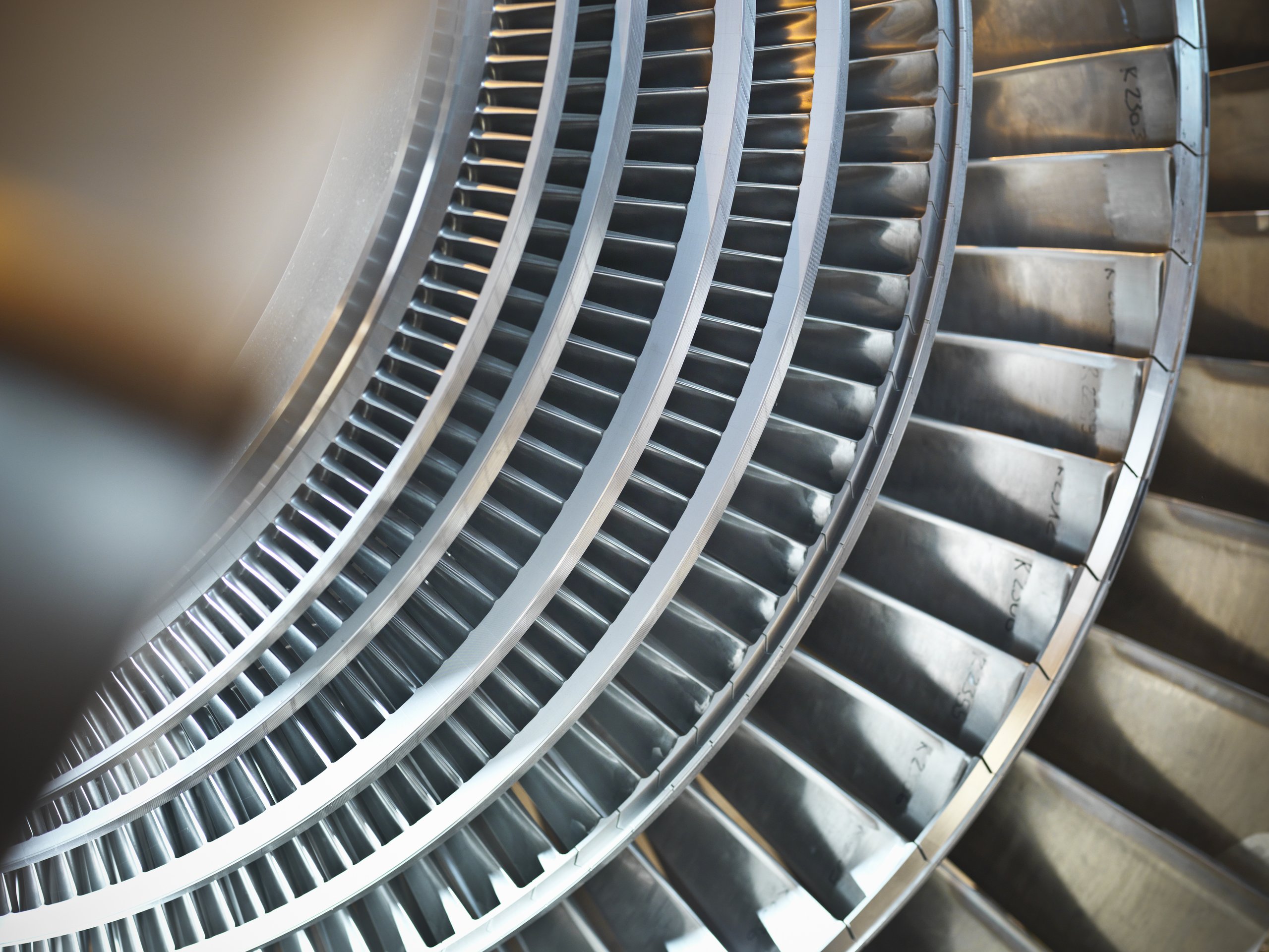 Close-up view of polished metal turbine blades arranged in concentric rings within an industrial energy generator.