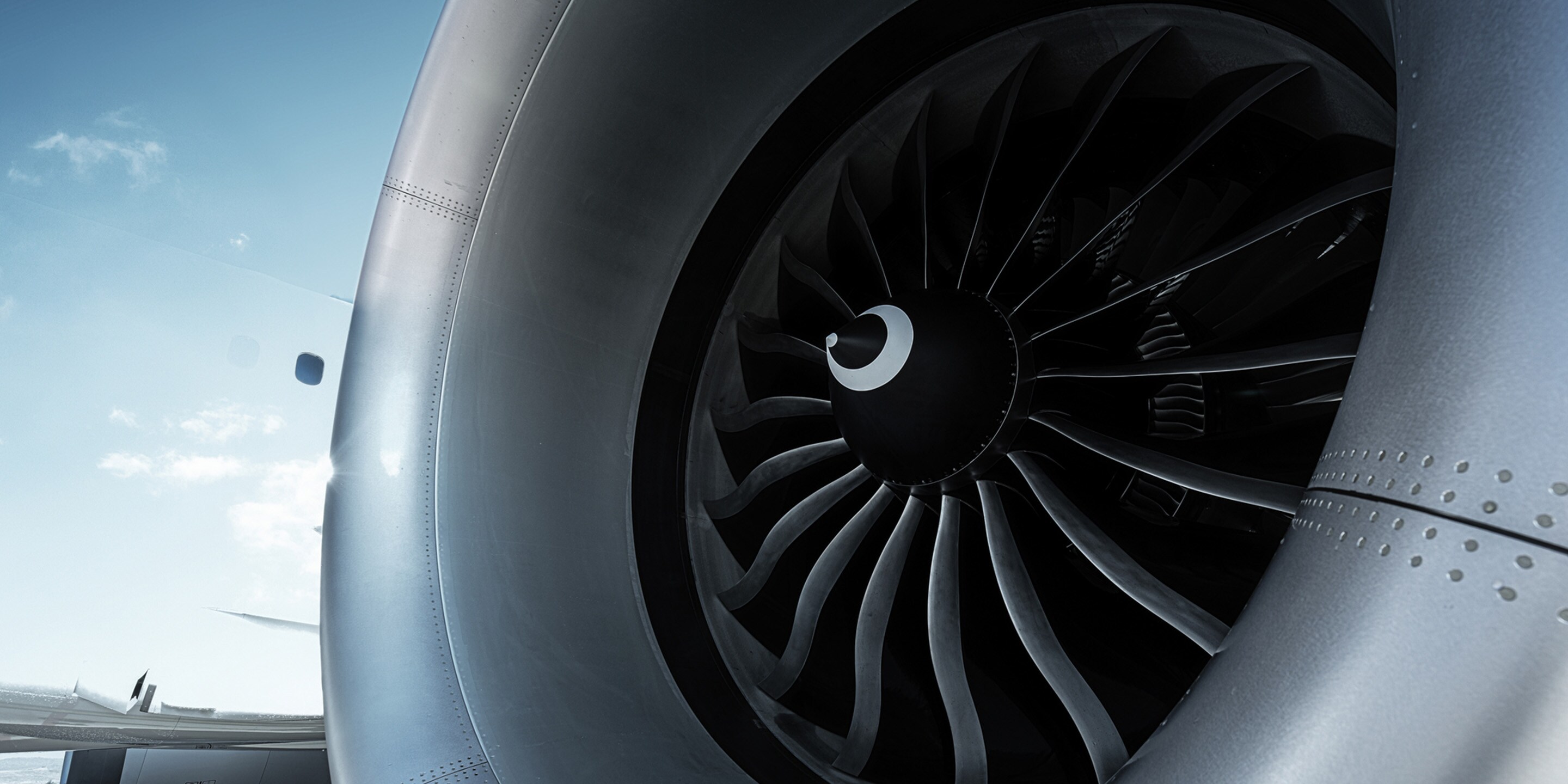 A detailed view of a jet engine fan blades, showcasing engineering precision and design against a clear blue sky backdrop.